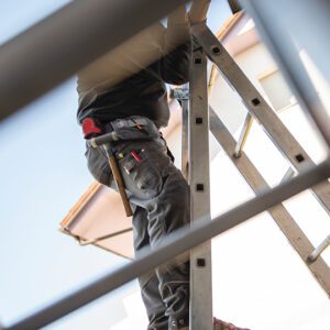 Worker on ladder with tools, viewed upward.